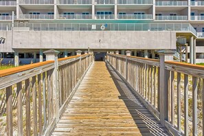 A wooden boardwalk leading to a building with multiple balconies and a concrete overhang. - Inviting Gulf-front condo In Perdido Key with waterfront pool/hot tub and oceanfront balcony (Perdido Key)
