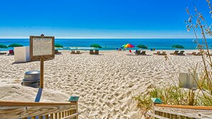 Une plage avec un panneau en bois, des chaises de plage et des parasols.