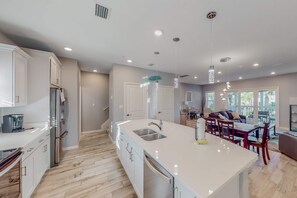 A modern kitchen with white cabinets, a large island with a sink, and a dining area with a table and chairs.