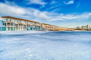 A row of beachfront buildings with balconies, a clear sky, and a road in the foreground.
