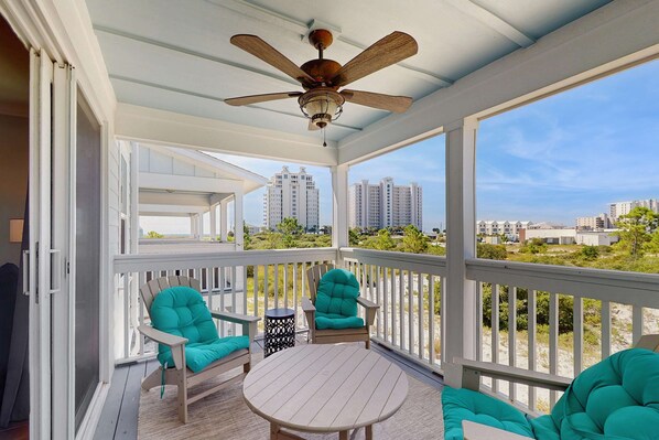 A covered outdoor seating area with a ceiling fan, white railings, and a view of distant buildings.