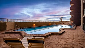 An outdoor swimming pool with lounge chairs, a palm tree, and a sunset view. - 4th-floor, bright, Gulf-front condo with views - close to entertainment (Fort Walton Beach)