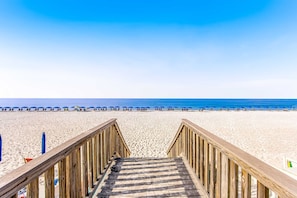 A wooden staircase leading to a beach with umbrellas and people in the distance. - Fourth floor oceanfront studio, balcony, full kitchen, heated outdoor shared pool, snowbirds welcome (Fort Walton Beach)
