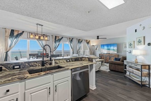 A modern kitchen with a large island, white cabinetry, and a built-in dishwasher. - Beachfront condo with gulf views, pool, gym, & private balcony (Fort Walton Beach)