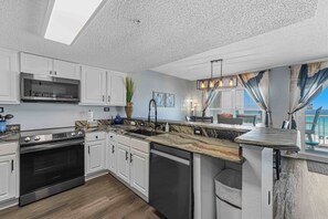 A modern kitchen with white cabinets, a stainless steel oven, a dishwasher, and a large window with a view. - Beachfront condo with gulf views, pool, gym, & private balcony (Fort Walton Beach)