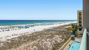 A beach view from a balcony with a pool, beach umbrellas, and a boardwalk. - Gulf front condo w/ beach setup included - near entertainment (Fort Walton Beach)