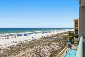 A beach view from a balcony with a pool, beach umbrellas, and a boardwalk. - Gulf front condo w/ beach setup included - near entertainment (Fort Walton Beach)