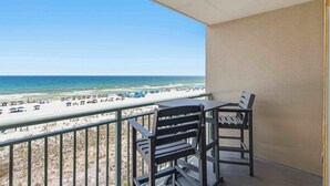 A balcony with a view of a beach, a table, and two chairs. - Gulf front condo w/ beach setup included - near entertainment (Fort Walton Beach)