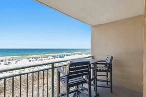 A balcony with a view of a beach, a table, and two chairs. - Gulf front condo w/ beach setup included - near entertainment (Fort Walton Beach)