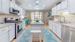 A modern kitchen with white cabinets, stainless steel appliances, a central island, and a blue patterned rug. - Home with kitchen, patio, playground, central AC, & W/D (Pensacola)