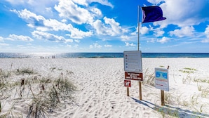 A beach with clear skies, a lifeguard flag, and warning signs about rip currents and no lifeguard on duty. - Home with kitchen, patio, playground, central AC, & W/D (Pensacola)