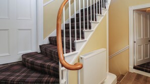 Una escalera con barandillas de madera y peldaños alfombrados con diseño escocés.