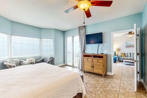 A bedroom with a bed, a ceiling fan, a TV, a wooden dresser, and a view of the living area through an open door. - Gulf-front resort condo w/ 2 on-site lagoon pools, hot tubs & beach service (Panama City Beach)