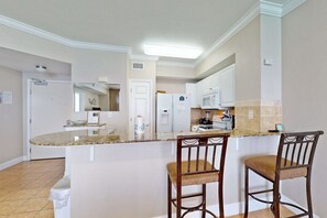 A kitchen with a granite countertop, two wooden bar stools, white cabinets, and a microwave. - 21st Floor Oceanfront Condo with Shared Pool & Hot Tub, Ocean View (Panama City Beach)
