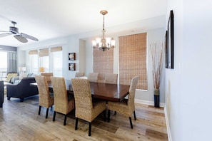 A dining area with a wooden table and wicker chairs, a chandelier, and a ceiling fan. - Chic & stylish beachfront condo with wraparound balcony, pools, & gym (Panama City Beach)