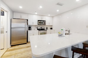 A modern kitchen with white cabinetry, stainless steel appliances, and a marble countertop. - Chic & stylish beachfront condo with wraparound balcony, pools, & gym (Panama City Beach)