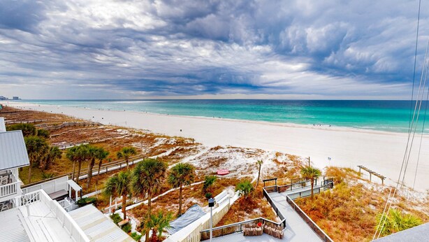 Blick auf einen Strand mit einem weißen Gebäude, sandigem Strand und bewölktem Himmel.