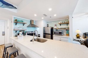 A modern kitchen with white countertops, stainless steel appliances, and a large island with stools. - Beachfront condo with a private balcony, three pools, tennis, & picnic area (Panama City Beach)