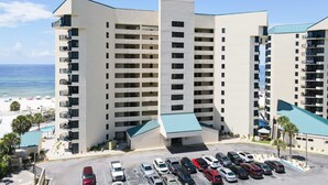 Ein mehrstöckiges Hotel mit Parkplatz, Poolbereich und Blick auf den Strand.