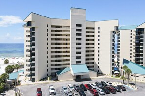 A multi-story hotel with a parking lot in front, a pool area, and a view of the beach. - Beachfront condo with a private balcony, three pools, tennis, & picnic area (Panama City Beach)