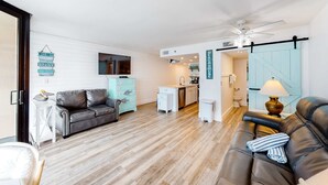 Ein modernes Wohnzimmer mit einer Couch, einem Couchtisch und einem Essbereich, im Hintergrund ist eine Küche zu sehen.