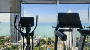 A gym with exercise equipment and a large window offering a view of a cityscape and a body of water. - 1 BR 5mins to beach Sea view Riviera Wongamat (Muang Pattaya)