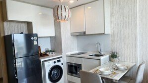 A modern kitchen with a stainless steel refrigerator, a built-in washing machine, and a dining area with a table set for two. - 1 BR 5mins to beach Sea view Riviera Wongamat (Muang Pattaya)