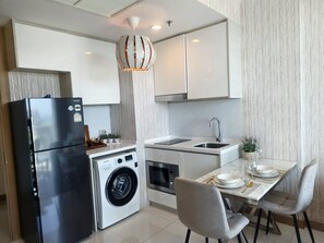 A modern kitchen with a stainless steel refrigerator, a built-in washing machine, and a dining area with a table set for two. - 1 BR 5mins to beach Sea view Riviera Wongamat (Muang Pattaya)