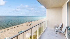 Een balkon met uitzicht op een strand, inclusief ligbedden en parasols.