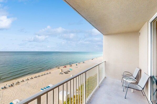 A balcony with a view of a beach, including lounge chairs and umbrellas. - Spacious, beachfront condo w/shared gym, sauna, hot tub, pools, and BBQ area (Panama City Beach)