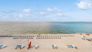 Een strand met rijen ligbedden en parasols, een redershut en een helder uitzicht op de zee.