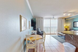 A hotel room with a dining area, a TV, a balcony with a view, and a trash bin. - Spacious, beachfront condo w/shared gym, sauna, hot tub, pools, and BBQ area (Panama City Beach)