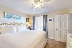 A bedroom with a bed, a ceiling fan, a window with curtains, and a door. - Spacious, beachfront condo w/shared gym, sauna, hot tub, pools, and BBQ area (Panama City Beach)