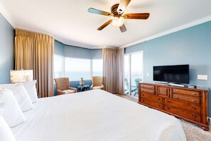 A hotel room with a large bed, a wooden dresser, a television, and a balcony with a view of the ocean. - Inviting gulf-front condo w/ beach service, pools, hot tubs & fitness center (Panama City Beach)