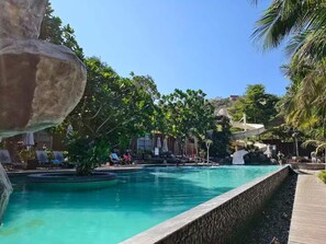Ein Poolbereich mit einer großen Felsformation, Liegestühlen und einer Wasserrutsche.