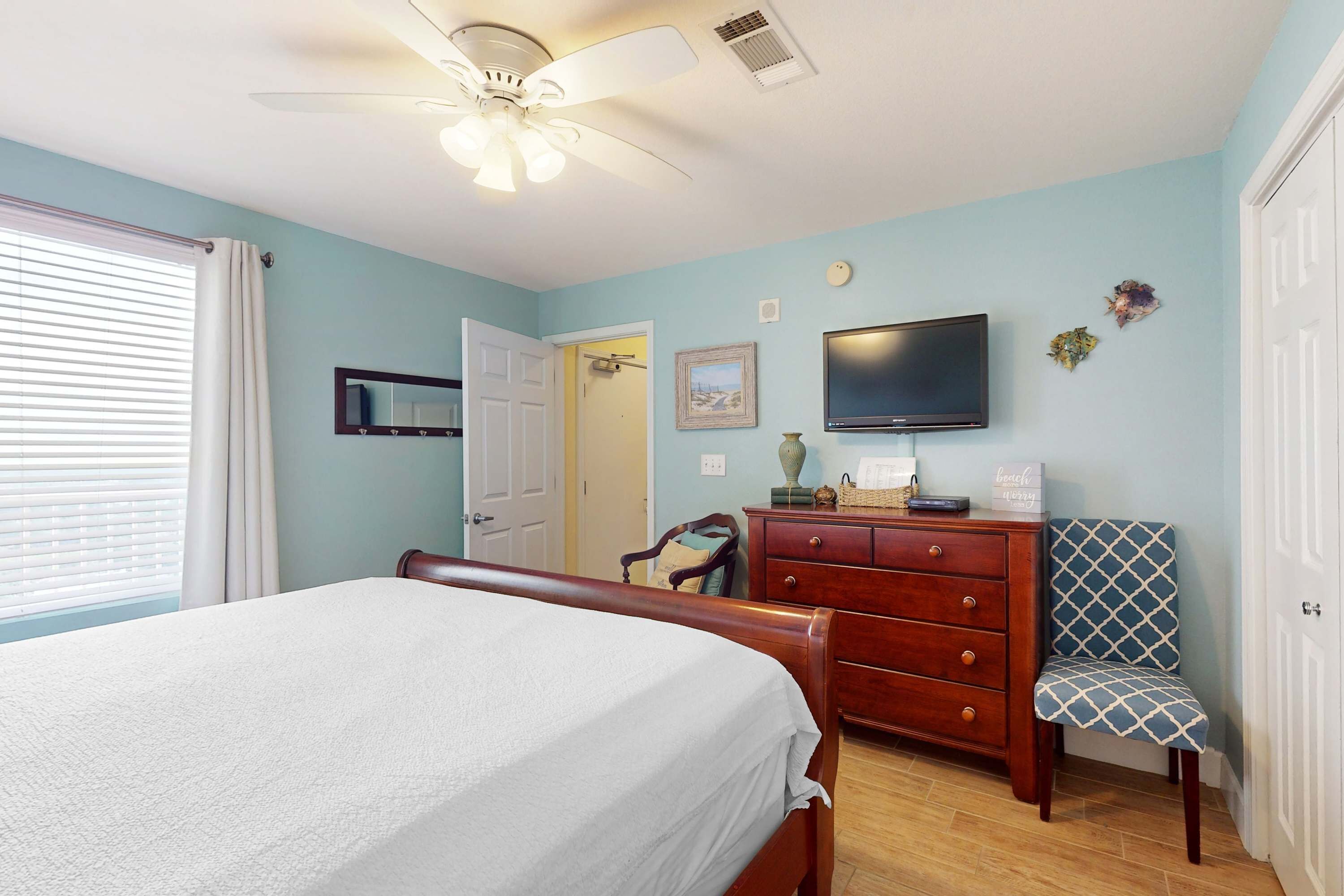 A bedroom with a bed, dresser, chair, television, and a ceiling fan.