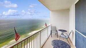 A balcony with a view of the ocean, a small table, two chairs, and an American flag. - 22nd-floor beachfront condo with Gulf views, hot tub, pools, sauna, gym, balcony (Panama City Beach)