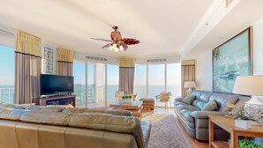 A spacious living room with a large sofa, a television, and a balcony with a view. - Spacious high-rise condo with stunning beachfront views, pools & hot tubs (Panama City Beach)