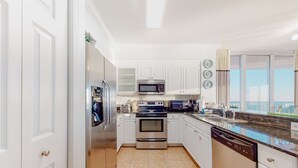 A modern kitchen with white cabinets, stainless steel appliances, and a view of the sea through large windows. - Spacious high-rise condo with stunning beachfront views, pools & hot tubs (Panama City Beach)