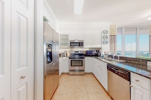 A modern kitchen with white cabinets, stainless steel appliances, and a view of the sea through large windows. - Spacious high-rise condo with stunning beachfront views, pools & hot tubs (Panama City Beach)