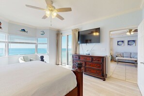 A bedroom with a large bed, a ceiling fan, a dresser, a TV, and a view of the ocean through the windows. - Oceanfront Condo with Shared Pool & Hot Tub, Ocean View, and High-Speed WiFi (Panama City Beach)