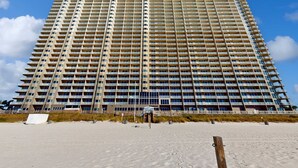 Un hotel de gran altura con varios pisos y balcones, ubicado en una playa de arena bajo un cielo despejado.