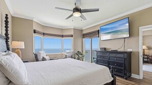 A bedroom with a large bed, a ceiling fan, a TV, and a view of the ocean. - Waterfront condo with furnished balcony, hot tub, pools & gym (Panama City Beach)