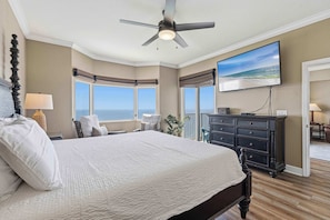 A bedroom with a large bed, a ceiling fan, a TV, and a view of the ocean. - Waterfront condo with furnished balcony, hot tub, pools & gym (Panama City Beach)