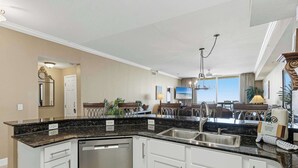 A kitchen with a built-in dishwasher, white cabinets, a granite countertop, and a stainless steel sink. - Waterfront condo with furnished balcony, hot tub, pools & gym (Panama City Beach)
