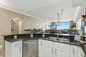 A kitchen with a built-in dishwasher, white cabinets, a granite countertop, and a stainless steel sink. - Waterfront condo with furnished balcony, hot tub, pools & gym (Panama City Beach)