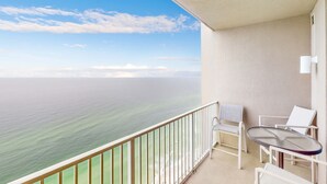A balcony with a view of the ocean, white chairs, and a small table. - Exquisite Gulf front condo w/shared pool, hot tub &, gym/Roman spa on-site (Panama City Beach)