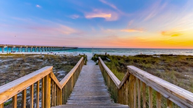 A wooden boardwalk leading to a beach with a pier in the background. - Exquisite Gulf front condo w/shared pool, hot tub &, gym/Roman spa on-site (Panama City Beach)