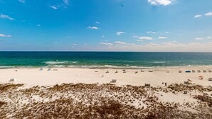 Ein Strand mit sandigem Ufer, einigen Sonnenschirmen und blauem Himmel.