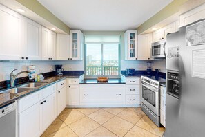 A modern kitchen with white cabinets, a stainless steel refrigerator, and a window with a view of a balcony. - 7th-floor, Gulf-front condo with views - close to dining (Perdido Key)
